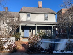 A gray, two-story colonial house with a  white fence.